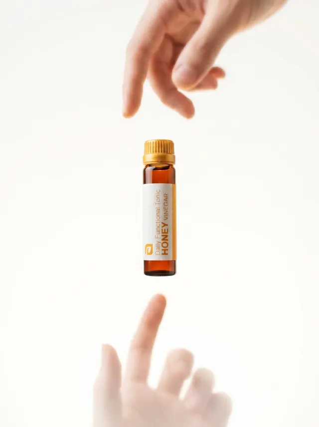A vial of Honey Vinegar passed between two hands