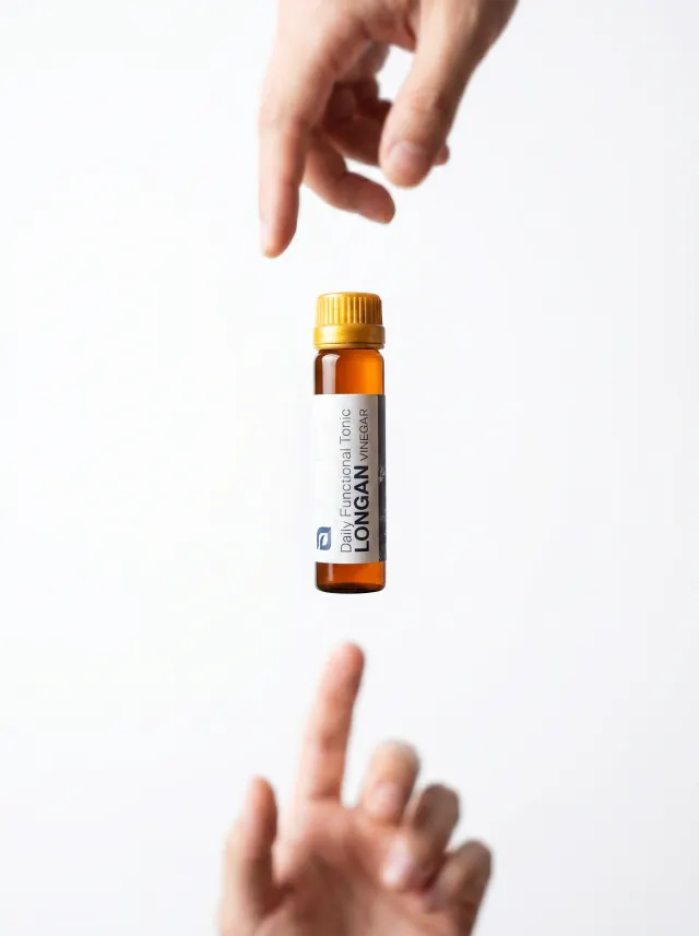 A vial of Longan Vinegar passed between two hands